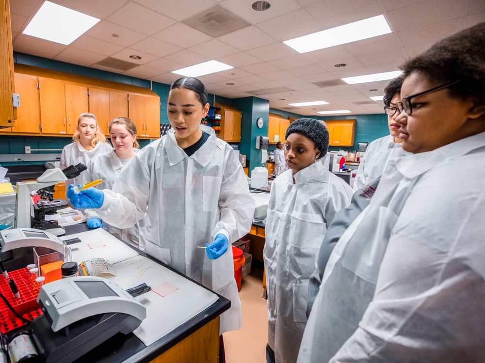 MLS graduates teaching high school students how to perform a urinalysis are, from left, Lakia Jones, Lauren Williams and Elizabeth Echols.