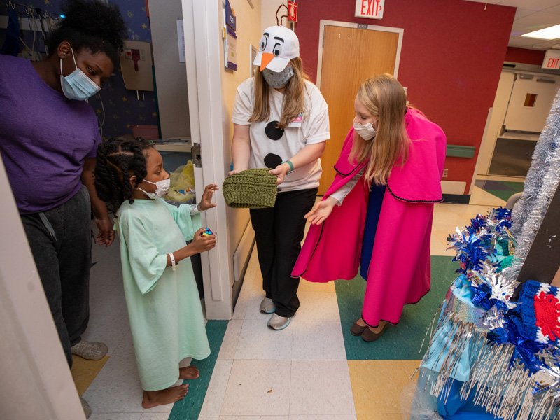 Children's of Mississippi patient Zayd Simmons of Conroe, Texas, gets a winter cap from "Olaf" and "Anna," aka child life specialist Courtney Easterday and medical student Anna Margaret Pitts, in the children's hospital's Thanksgiving Parade Nov. 22.