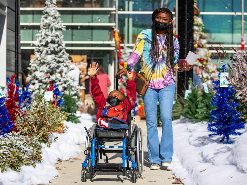 Children's of Mississippi patient Roderick Lynn tries to catch flakes from a snow machine as his mother, Tamara Morton, pushes him through BankPlus Presents Winter Wonderland.