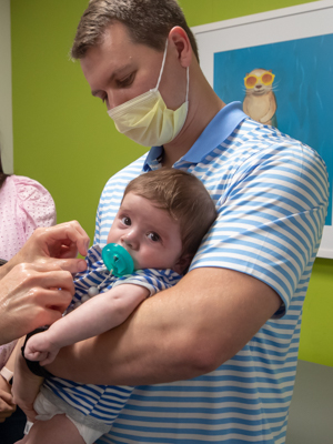 Stephen Sims of Hattiesburg hold son Bishop as Dr. Phillip Burch prepares to examine the heart surgery incision on Bishop's chest. Jay Ferchaud/ UMMC Communications 