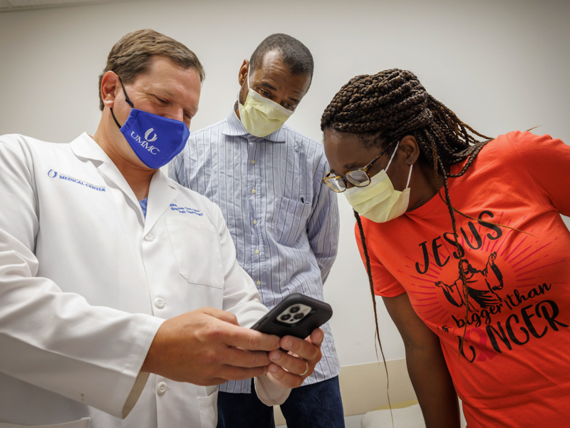 Orr, left, shows patient Darrell Freeman and Freeman's fiancee, Tonya Johnson, photos taken during Darrell's HIPEC surgery. Joe Ellis/ UMMC Communications