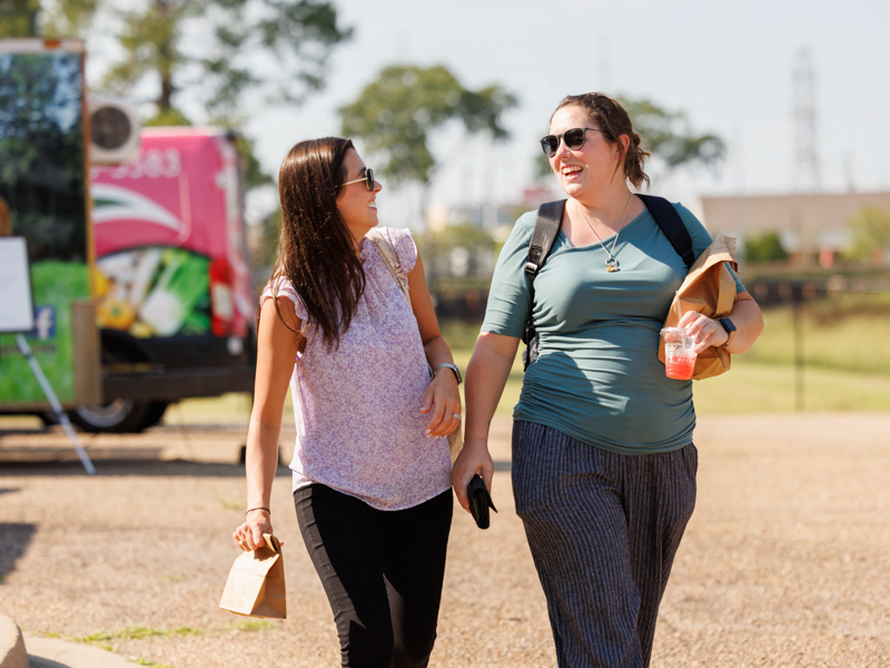 Lauren Greenlee, left, and Nicole Connolly, both admissions officers with Student Services and Records, leave Thursday afternoon's Farmer's Market behind Backyard Burger with bags of goodies. The event was sponsored by the UMMC Office of Well-being. Joe Ellis/ UMMC Communications 