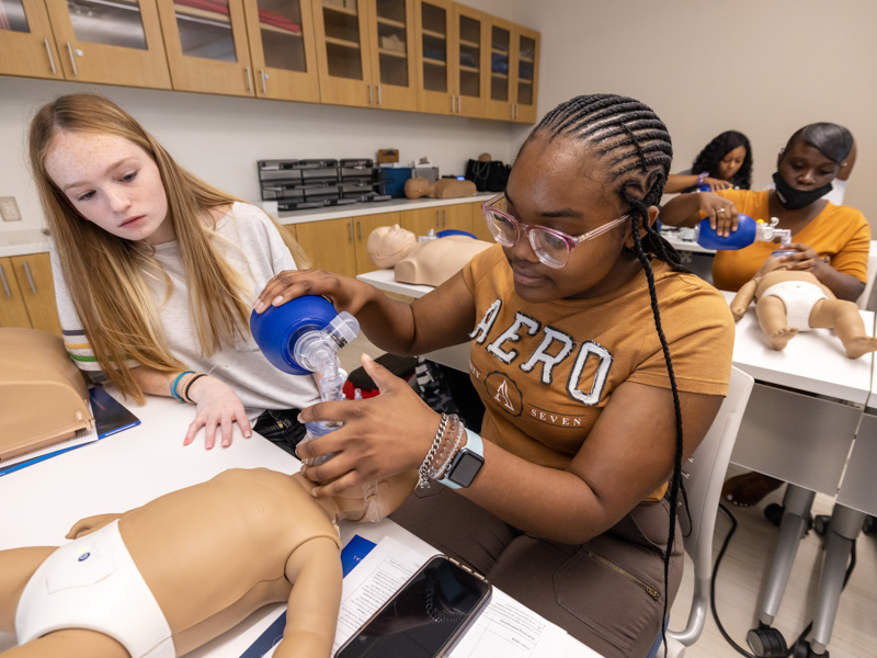 Practicing together on an infant-size mannekin, Emma Rhodes, 16, left, a rising senior at Kosciusko High School, and Deundra Wilson, 15, who will be a junior at Holmes County Central High School in Lexington, are absorbed by the functions of the self-inflating bag valve mask, a life-saving device for patients who are not breathing or not breathing adequately. Jay Ferchaud/ UMMC Communications 