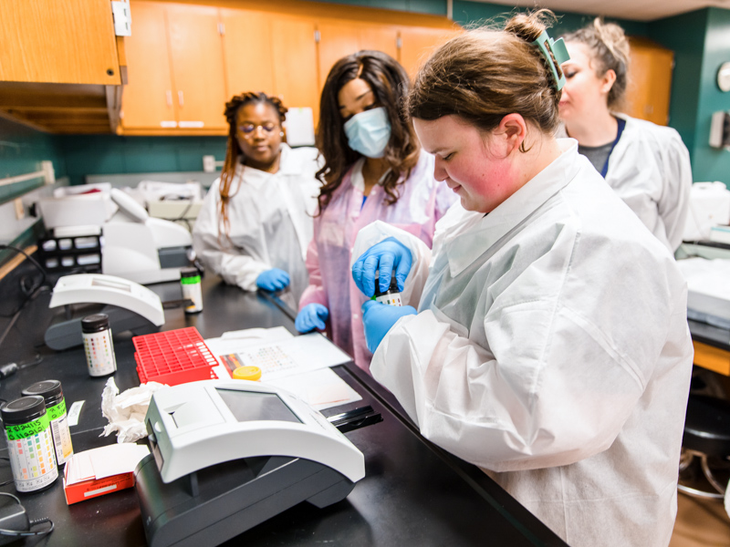 Medical Laboratory Science student Madison Alford tests a urine sample with the help of Dr. Stacy Vance, while classmates look on.
