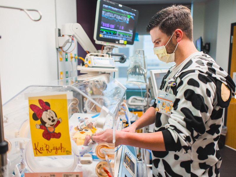 NICU nurse Houston Strength, wearing a cow costume for the unit's barnyard Halloween theme, checks on patient Kei'Riyah Leonard. Lindsay McMurtray/ UMMC Communications