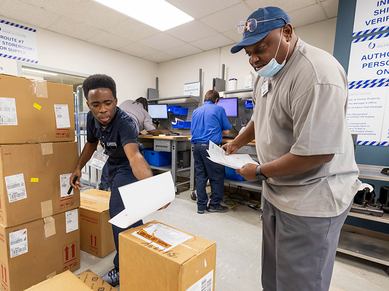 Shipping and Receiving Supply Techs Kierston Deloach, left, and Sheldon Perry match up receipts with orders as Supply Tech Kenan Jackson and Supervisor Cory Spooner process orders electronically in the warehouse.
