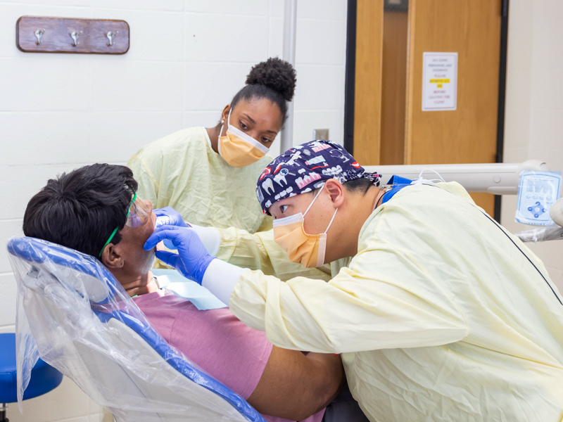 Third-year dental student Cedar Baik, right, examines patient Beverly Diamond with assistance from Ashley Arnold, a fourth-year dental hygiene student.
