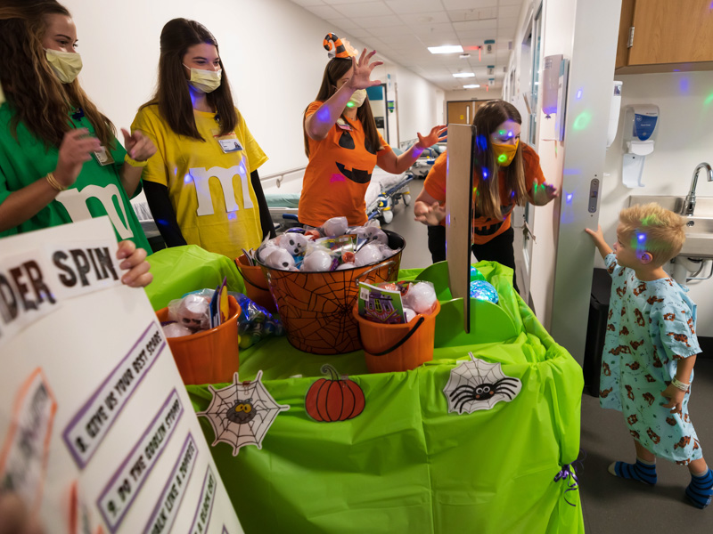PediaRebs members and pharmacy students, from left, Izzabella Christian, Emily Nichols and Carly Cappleman, and child life specialists Cara Williams and Courtney Easterday bring reverse trick-or-treating to Children's of Mississippi patient Jett Jenkins of Clinton. Melanie Thortis/ UMMC Communications 