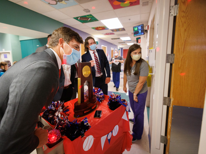 Ole Miss baseball players including Brandon Johnson, left, and Hunter Elliott paid Children's of Mississippi patients a surprise visit Thursday, letting patients get a look at their 2022 College World Series trophy. Beside them is child life specialist Cara Williams. Joe Ellis/ UMMC Communications