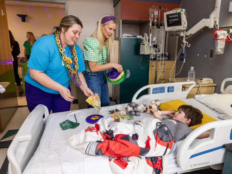 Children's of Mississippi patient Waylon Bilbro of Morton gets Mardi Gras goodies from Allyson Holliman, left, and Janna Lampton, a board member of Friends of Children's Hospital. Jay Ferchaud/ UMMC Communications 