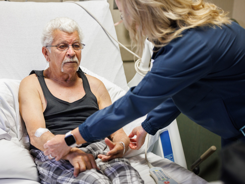 Following instructions from UMMC neurologist Dr. Juebin Huang during a telehealth visit, South Central Regional Medical Center patient Michael Bustin allows neurology nurse practitioner Delane Pressly to gently touch his hands and arms.