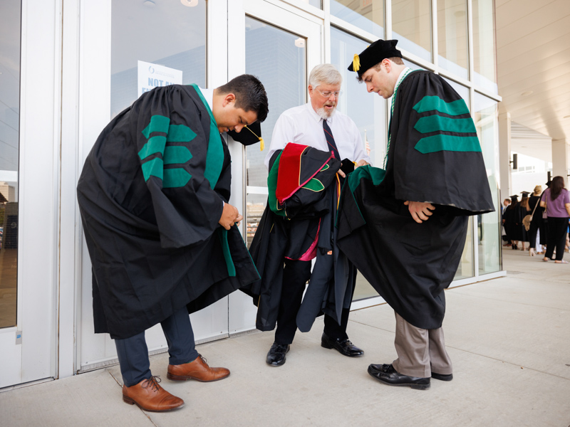 From left, Mitchell Ostrander, assistant professor of medicine; Dr. Scott Berry, assistant professor of surgery and father of School of Medicine graduate Hunter Berry, right, prepare for commencement.