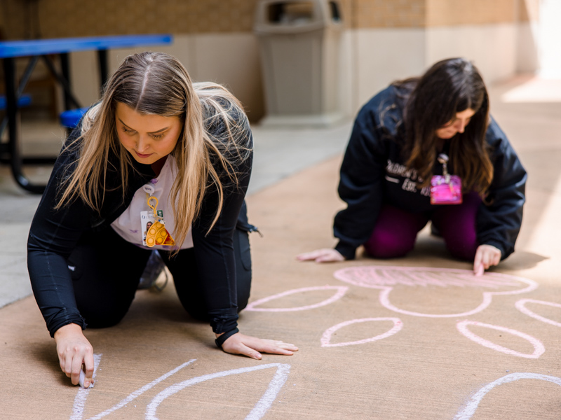 Allyson Holliman, left, and child life specialist Kelsey Clark work on a sidewalk chalk greeting for Mississippi State's baseball team. Lindsay McMurtray/ UMMC Communications 