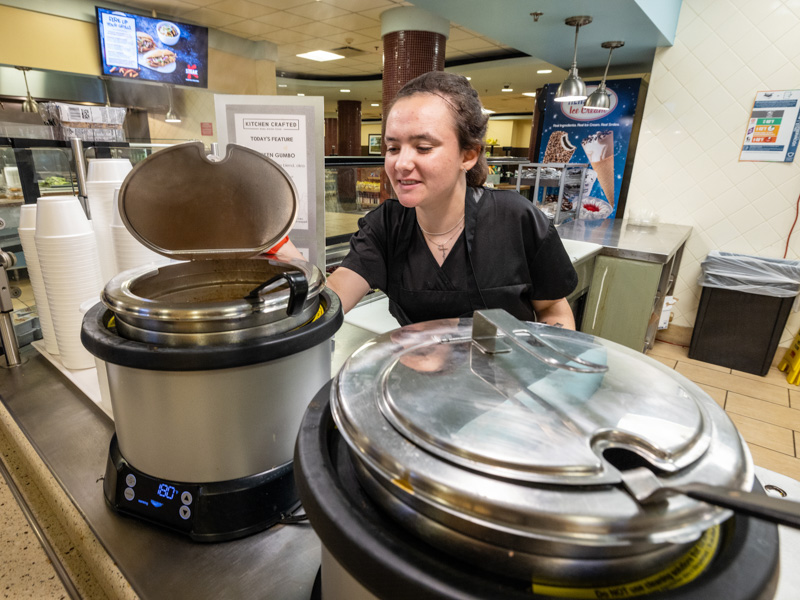 Program SEARCH graduate Reilly Easley checks a pot of soup on the job with Morrison Healthcare food service at the UMMC cafeteria.