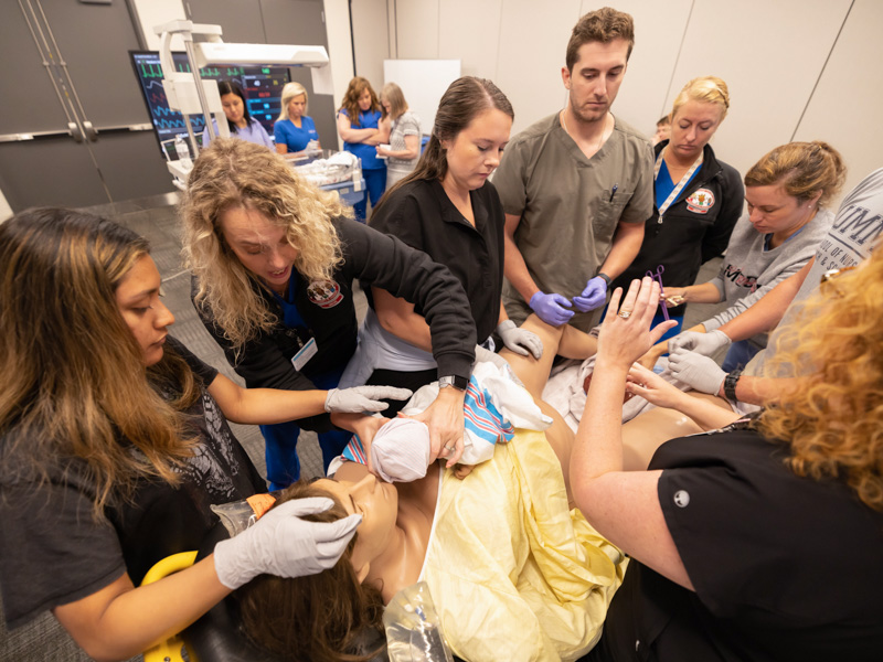 A simulated newborn is handed off to Mirzait Sanchez, left, a recent East Central Community College nurse graduate, and AirCare pediatric transport nurse practitioner Emily Wells. Assisting with the "birth" are Children's of Mississippi PICU nurses Sarah Vaughan, Ben Tarver and Simone Willis; and maternal-fetal specialist Dr. Rachael Morris.