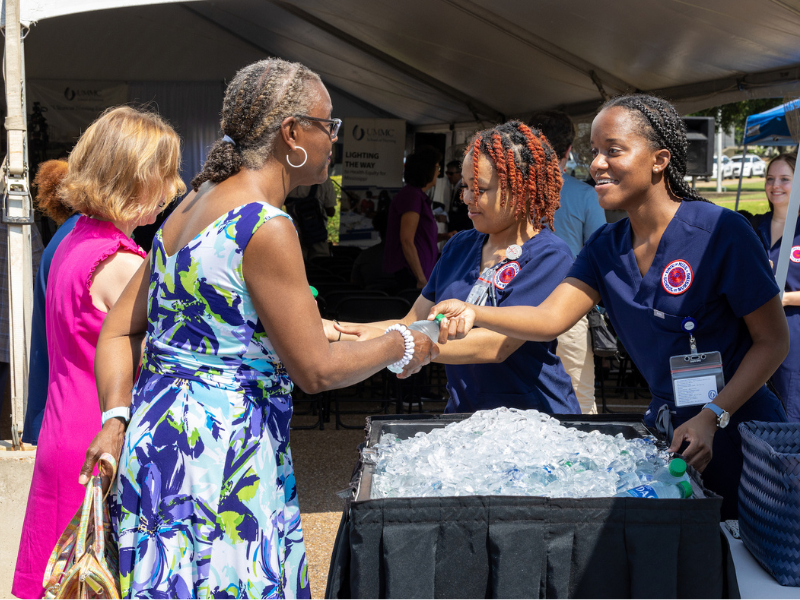 Nursing student and GivePulse volunteers Chassidy Rogers, left, and Kayla Evens pass out water and programs during the UMMC School of Nursing groundbreaking.