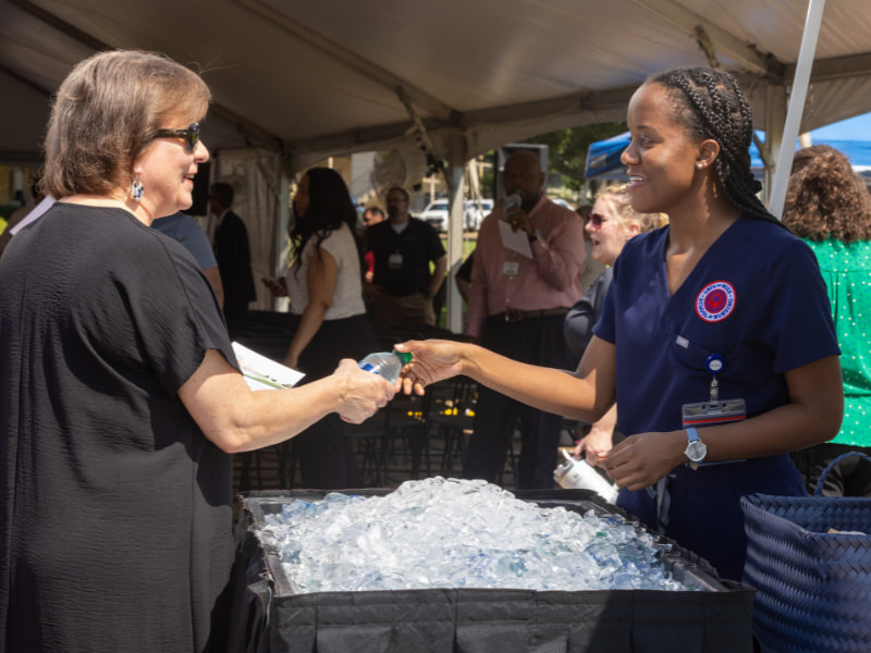 Kayla Evans, right, a first-year nursing student, hands a bottle of water to Nancy Ladd, education administrator for the Office of Academic Affairs, at a groundbreaking ceremony held June 28 for the new School of Nursing. Evans was among several student volunteers working the event.