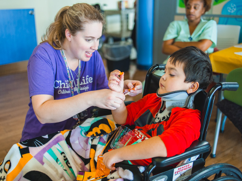Child life specialist Madeline Wilson helps patient Cross Wilson of Magnolia put on a glow stick bracelet.