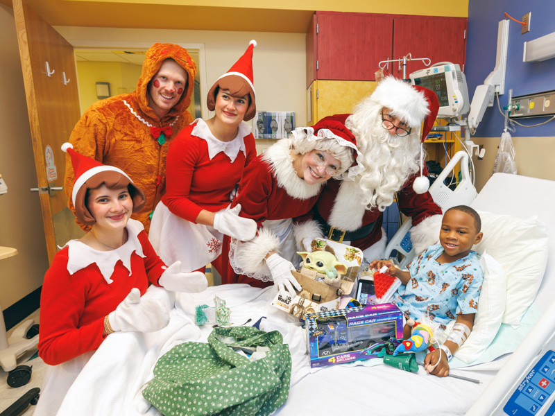 Children's of Mississippi patient Eric Bingham II of Vicksburg smiles with Santa and Mrs. Claus, elves and the gingerbread man. Jay Ferchaud/ UMMC Photography