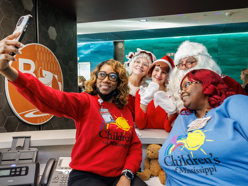 Candias Johnson, patient data access integrity specialist, takes a selfie with Sandra Collier, access financial coordinator, and a few visitors from the North Pole. Jay Ferchaud/ UMMC Photography