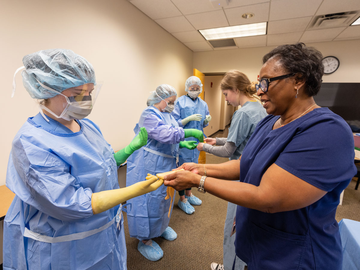 A group of M3's, including Selah Hall, left, foreground, undergo scrub training under the direction of, among others, Joyce Shelby, right, director simulation operations in the School of Medicine. The training was part of this summer's M3 Boot Camp, when students begin their clinical training in earnest on the road to choosing a specialty. Jay Ferchaud/ UMMC Photography