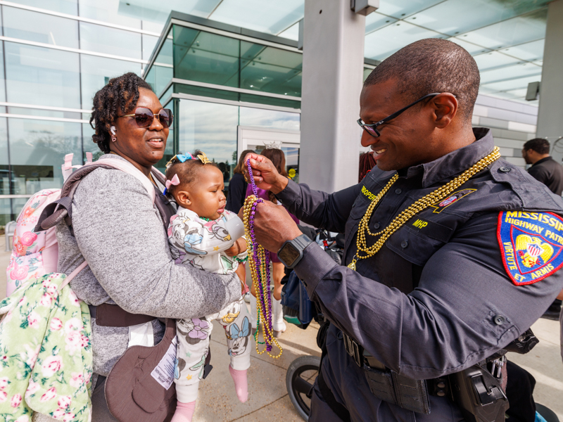 A Mississippi Highway Patrol officer Aaron Spann delivers Mardi Gras beads to Madelyn Bush, held by her mom, London Williams-Bush.