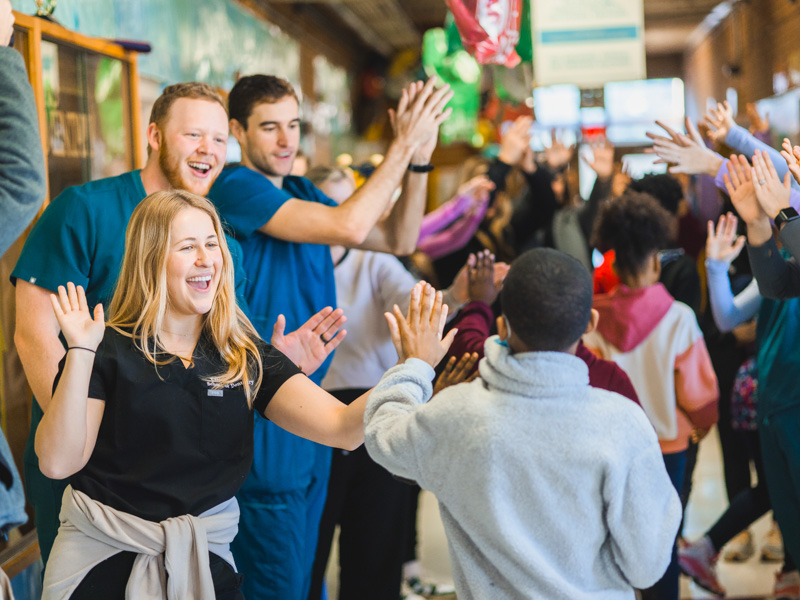 Dental students Emison Geiger, Dutton Day and Dalton Thompson high-five Wilkins Elementary students on their way to Give Kids a Smile Day.