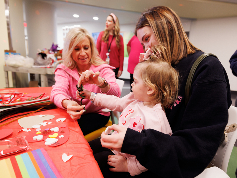 Maj. Nancy Porter helps Children's of Mississippi patient Adley Thomas of Rayville, Louisiana, with a Valentine's Day craft. Holding Adley is her mom, Madison. Jay Ferchaud/ UMMC Photography