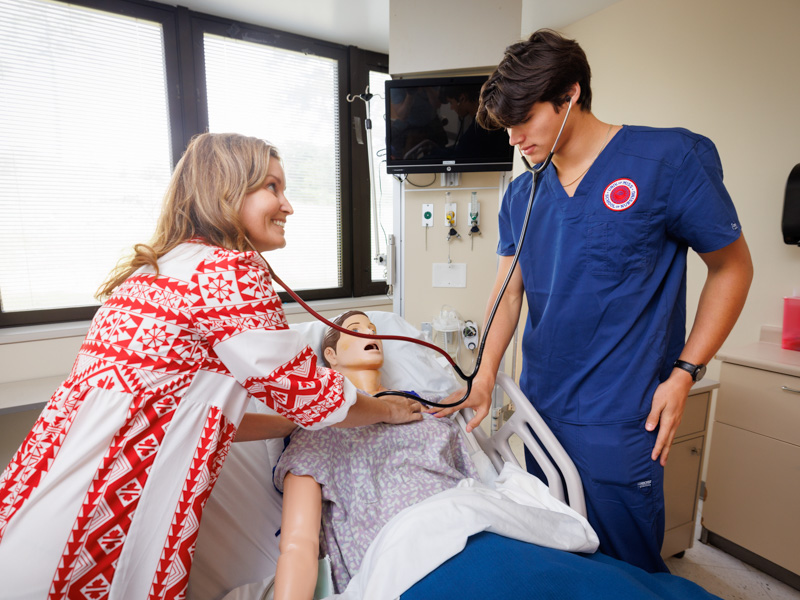 Dr. Amanda Weeks, director of simulation, assists nursing student Elijah Barberi in health assessment.