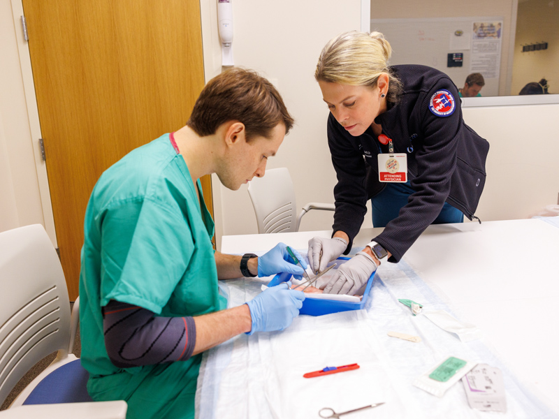 Dr. Risa Moriarty, assists new emergency medicine resident Jacob Meyer in suturing. Jay Ferchaud/ UMMC Communications 