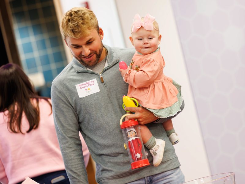 Children's of Mississippi patient Tatum Smith, held by her father, peeks at holiday surprises at Santa's Workshop. Melanie Thortis/ UMMC Communications