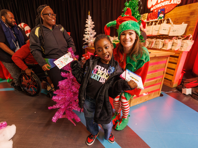 Arielle Mitchell of Pascagoula smiles with a volunteer elf during BankPlus Presents Winter Wonderland and Ace Tree Farm. Melanie Thortis/ UMMC Communications