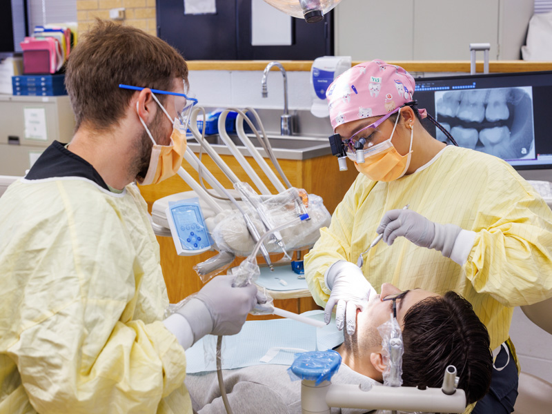 Dental students Nguyen (D4) and Hunter Holley (D2) prepare patient James Berggren Jr.—Nguyen’s husband—for a crown.