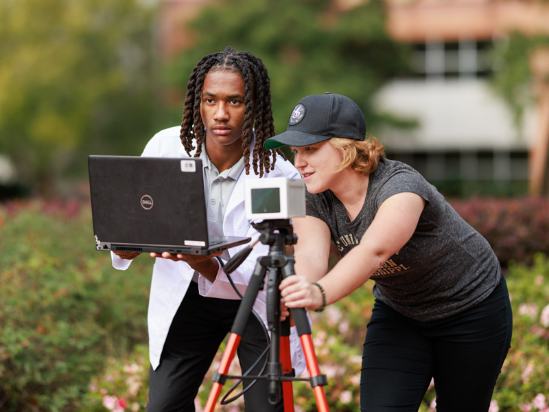 Hattiesburg High Base Pair student Maurice Sutton, left, works with Dr. Kayla Stan, University of Southern Mississippi assistant professor of geography, to research using a 3D scanner perched atop a tripod stand on the university campus.