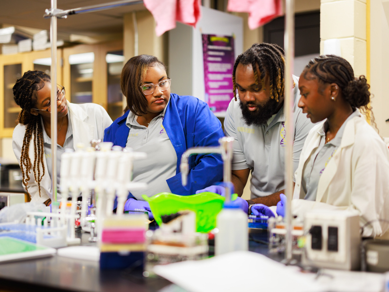 Dr. Kendrick Buford, second from right, works with Hattiesburg High students, from left, Kendall Ellis, Wynter Fairley and Logan Hughes to resolve some quirks in their research at the school laboratory.