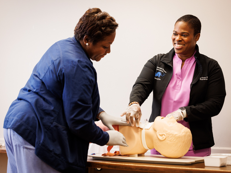 Liza Owens and Levonne Wiley, clinical education and outcomes coordinator for respiratory therapy, work with a manikin