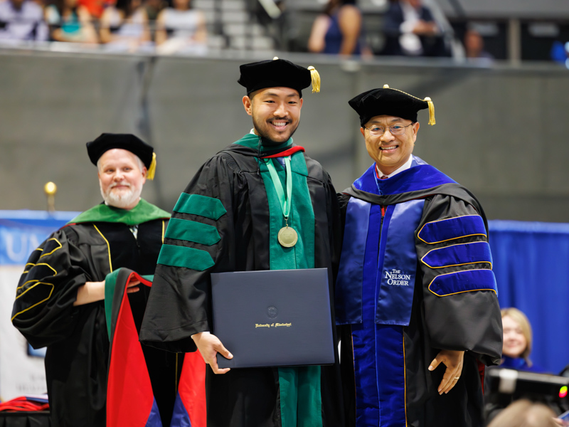 Doctor of Medicine recipient Wesley Zhang is hooded by his father, Lei Zhang, associate dean for research and scholarship, professor and Harriet G. Williamson Endowed Chair for Population Health Nursing. Melanie Thortis/ UMMC Communications