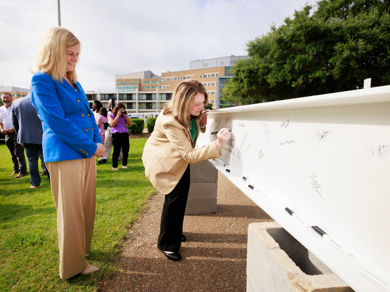 Dr. Tina Martin, dean of the UMMC School of Nursing, watches as Dr. Natalie Gaughf, assistant vice chancellor for academic affairs at UMMC, signs the beam. Joe Ellis/ UMMC Communications