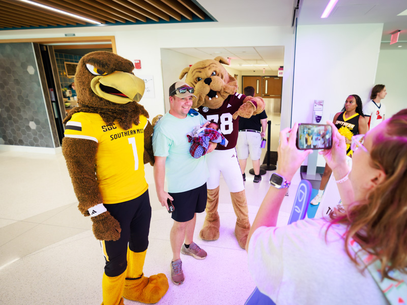 Justin Kentfield holds patient Luca Embry of Meridian while wife Ashley snaps a photo of them with Seymour and Bully, the mascots for the University of Southern Mississippi and Mississippi State University, respectively. Joe Ellis/ UMMC Communications