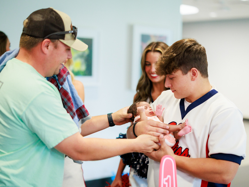 Justin Kentfield places Children's of Mississippi patient Luca Embry of Meridian in the arms of Ole Miss cheerleader Lake Saik. Joe Ellis/ UMMC Communications
