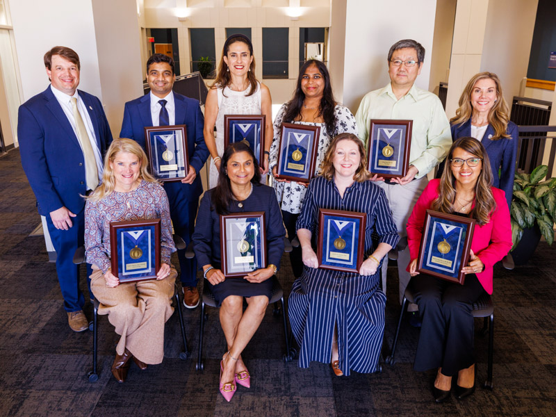Dr. Lee Bidwell, left, associate vice chancellor for research, and Dr. Caroline Compretta, right, assistant vice chancellor for research, congratulate bronze medallion winners, seated, from left, Dr. Lisa A. Haynie, professor of nursing; Dr. Seema Singh, professor of cell and molecular biology and CCRI associate director of education and training; Dr. Cynthia Karlson, professor of pediatrics; Dr. Susana M. Salazar Marocho, associate professor of biomedical materials science; and standing, Dr. Pradeep K. Vaitla, medical director of kidney-pancreas transplantation; Dr. Ana T. Palei, associate professor of research in the Department of Surgery; Dr. Lavanya Challagundla, assistant professor of cell and molecular biology; and Dr. Yufeng Zheng, associate professor of research in the Department of Data Science.