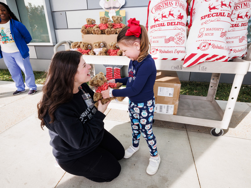 Kelsey Clark, Child Life Specialist, gives a teddy bear to Lydia Jarreau, 4, of Ruth, donated by Nicholas Air. Jay Ferchaud/ UMMC Communications