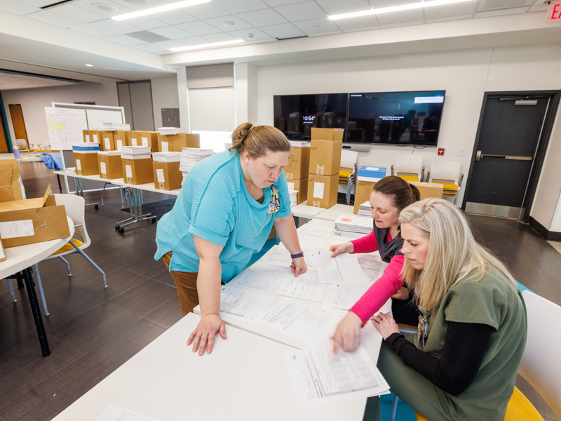 Olivia Ulbrich, project manager for child life, Shanna Kennon, shift supervisor at the Clarke Center, Brittany Harwell, clinical outcomes coordinator at the Clarke Center meet in the Kathy and Joe Sanderson Tower community room to put together binders of paperwork to be used at the Clarke Center.