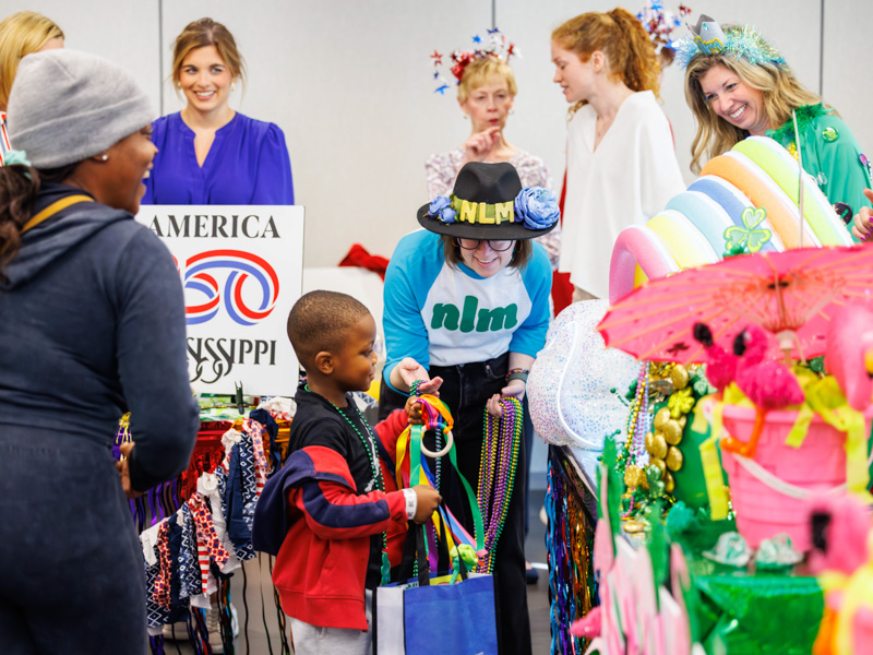 Jireh Bryant, 4, of Jackson, with his mom Candice Bryant, gets beads from Sophie McNeil Wolf with the NLM krewe at the 2026 Petite Parade at the children's hospital. Melanie Thortis/ UMMC Communications