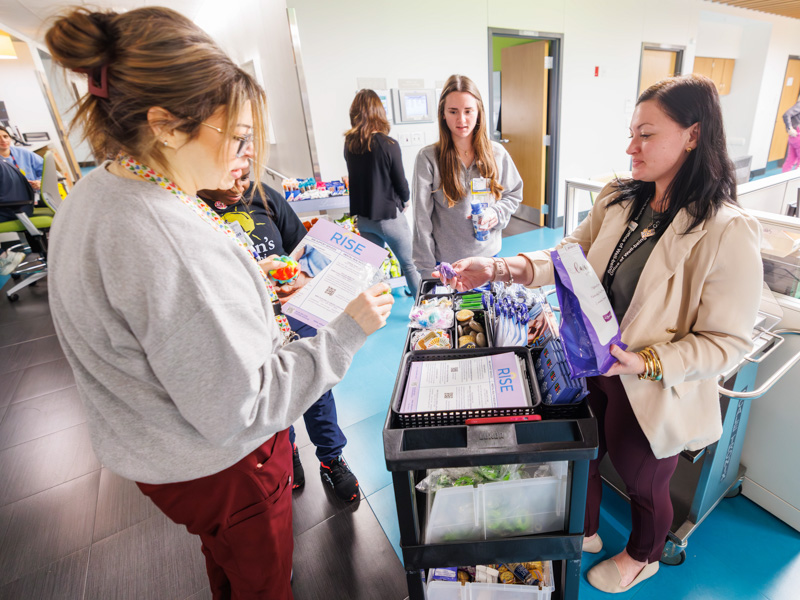 Samantha Smith, a social worker in the Office of Well-Being, right, passes out lavender bundles from the RISE Lavender Cart to PICU nurses, from left, Meghan Murphey, Karen Blair-Jackson and Mallory Watts.