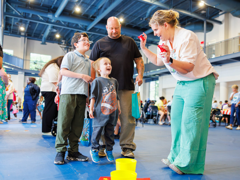 Ransom Paul, 4, alongside his family, jumps for joy with Ann Skelton, program director of mental health services, during the bean bag toss at the NICU reunion at the children's hospital.