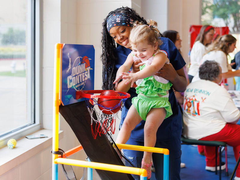 Emersyn Bracknell, 3, gets help from School of Nursing student Courtney Bilbro during the dunk contest part of the NICU reunion at the children's hospital.