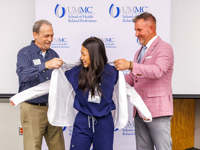 Radiologic Sciences program student Cindy Tran receives her white coat from Dr. Lee Brown, left, and SHRP Dean Jay Garner during orientation week. Jay Ferchaud/ UMMC Communications