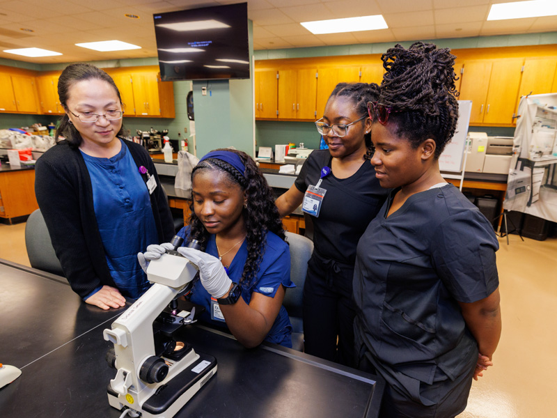 Yin Wang, assistant professor of medical laboratory sciences, left, with new students Mysheaira Taylor, Constance Harper and Jasmine Thompson check out slide samples during orientation week.  Jay Ferchaud/ UMMC Communications