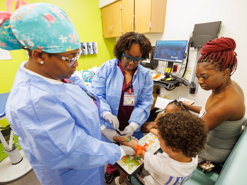 Children's of Mississippi Draw Station Clinical Lab phlebotomists Keyerica Taylor, center, and Chi'Keidreya Parker draw blood from patient Kaisinn James .